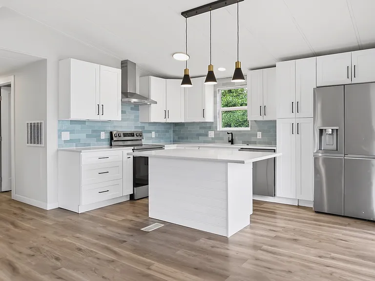 Kitchen with Blue Tile Backsplash, Stainless Range, Quartz Island, and Hallway to Bedrooms