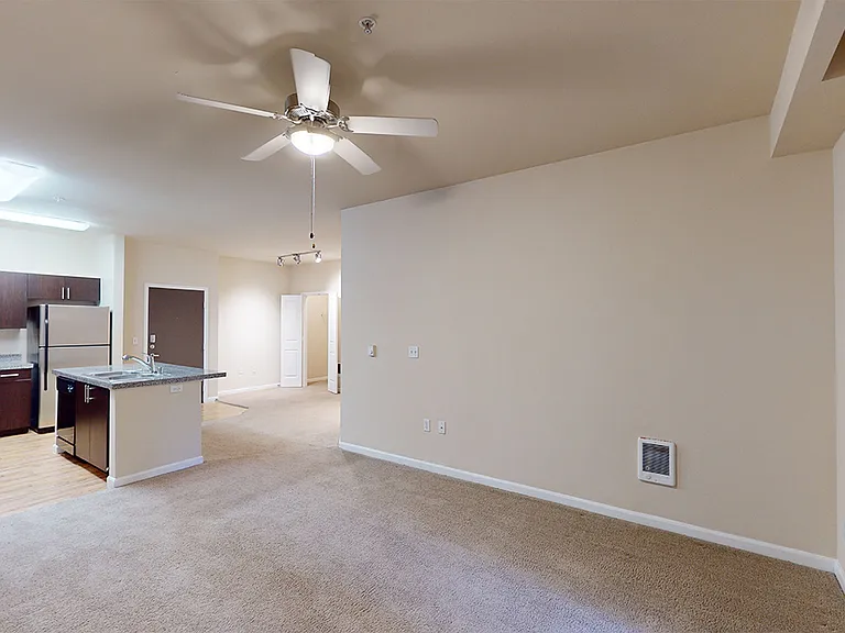 Apartment kitchen, dining and living room with plush carpet flooring.
