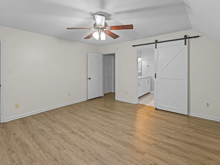 Spacious bedroom with stylish barn door entry, ceiling fan, and gleaming hardwood floors _ a serene retreat.