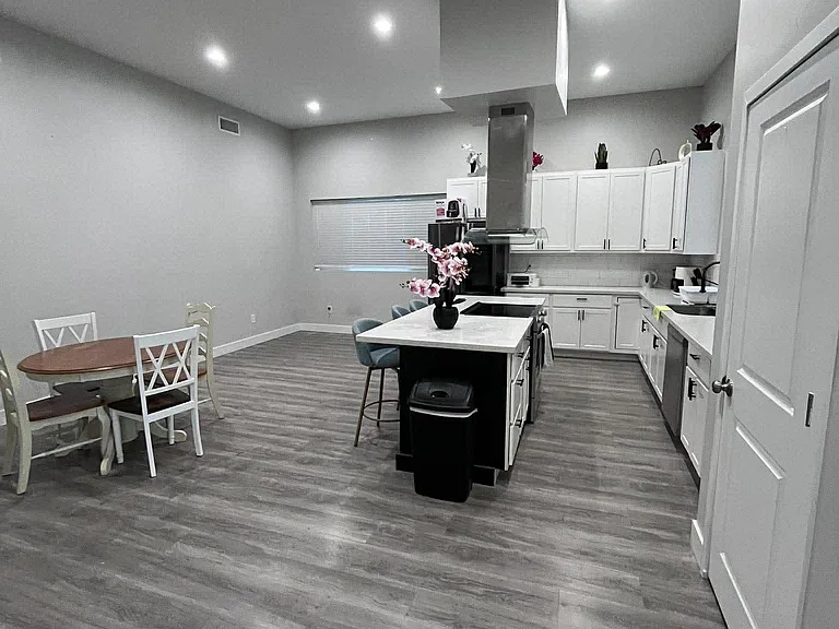 Open kitchen with large island, ample white cabinetry, and stainless appliances, plus space for a small dining set.