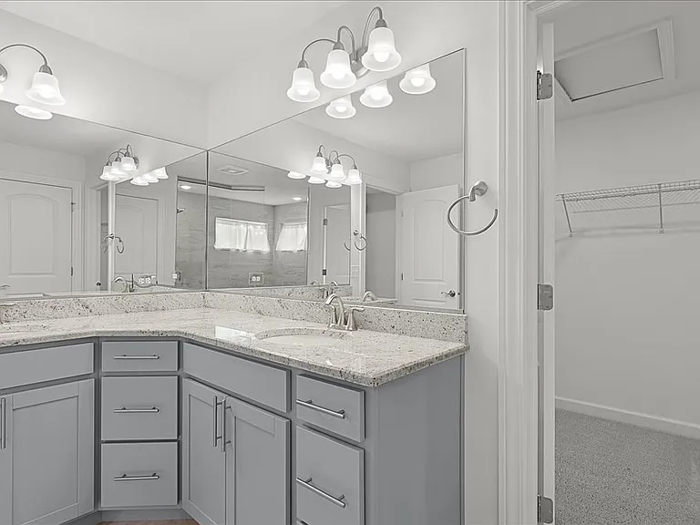 Primary bathroom with dual sinks, granite countertops, walk in shower, and walk in closet