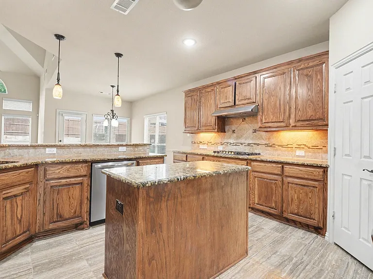 Kitchen featuring wood cabinetry, granite countertops, tile backsplash, and a central island