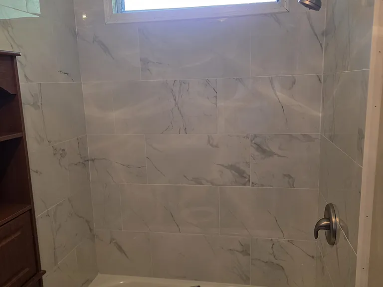 Full bath with tub and shower in back area and tile on 3 walls