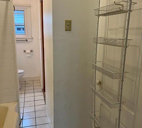 extra storage in bathroom with large porcelain bathtub and ceramic tiled floors