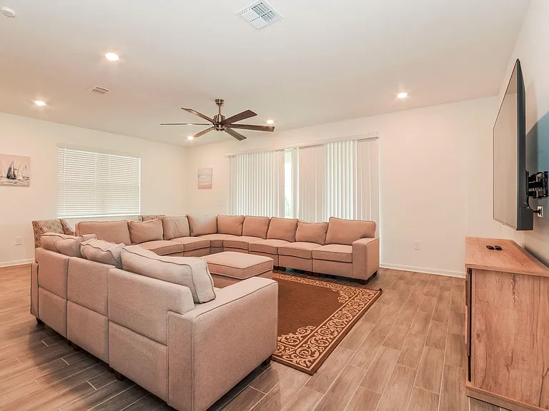 Spacious living room with a large sectional, ceiling fan, and wall-mounted TV, plus sliding doors for easy outdoor access.