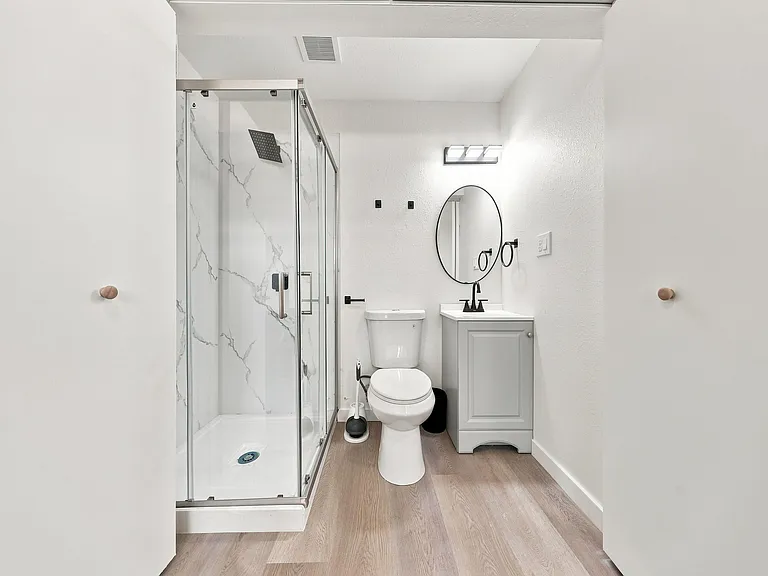 Updated full bath with glass-enclosed shower, marble-look surround, and a vanity with mirror and modern fixtures.
