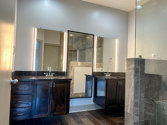 The master bath has wood tile floors with halogen lit mirrors. You can see the corner of the glassed in silver marble walk in shower.