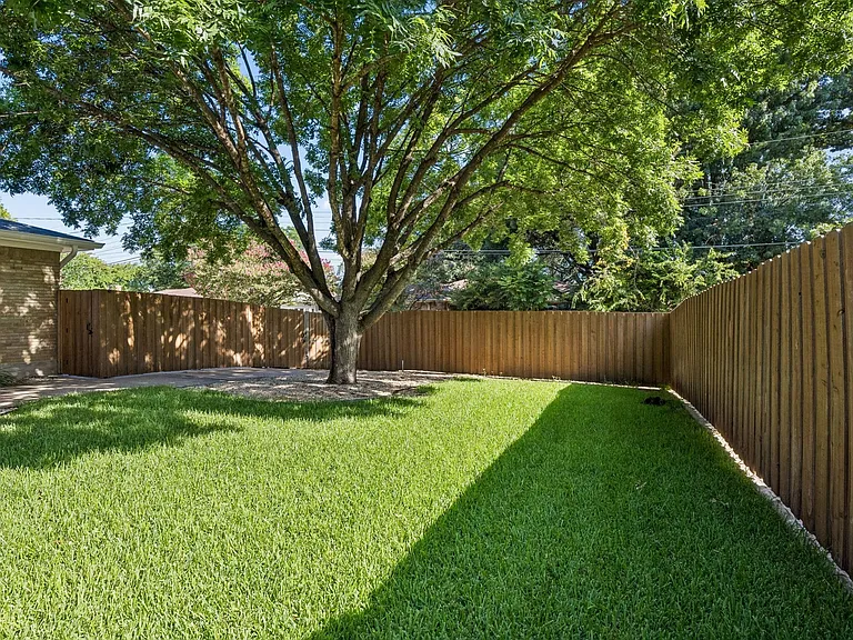 Expansive backyard featuring a mature shade tree, manicured lawn, full privacy fencing, and a gravel perimeter