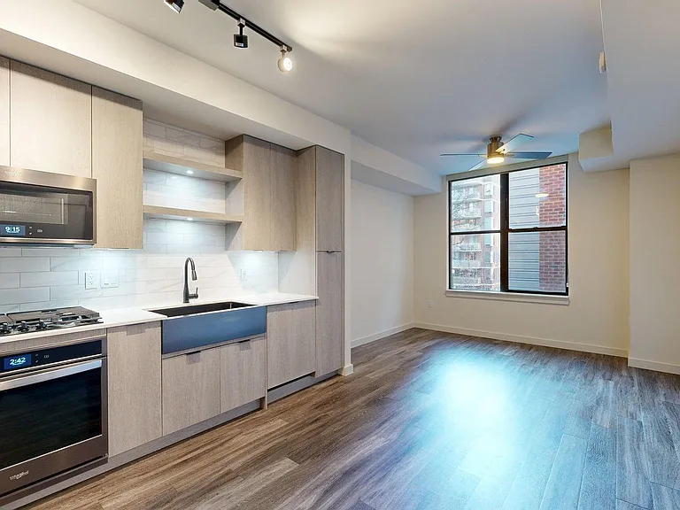 Apartment Kitchen with Stainless Steel Appliances, Dining and Living Room with Wood Style Flooring.