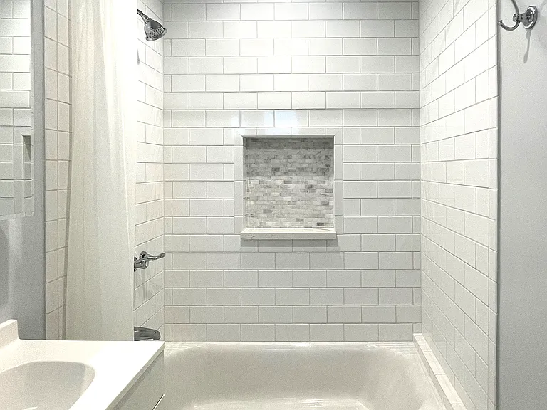Tumbled marble cubby in the bath tub with a shower.
