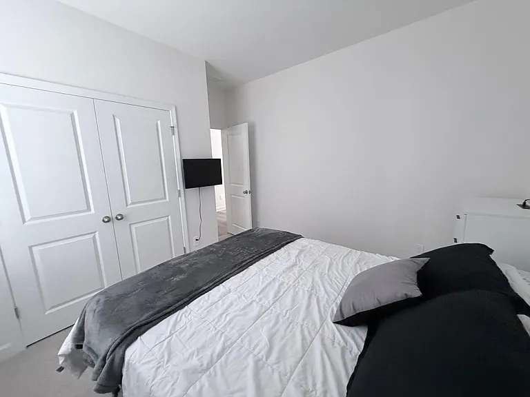 Neatly furnished bedroom with a comfortable bed, wall-mounted TV, and a double-door closet for convenient storage.