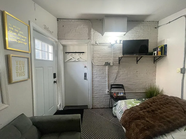 Private bedroom with painted brick accent wall, wall-mounted TV shelf, and space for a bed plus seating.