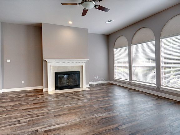 Spacious room featuring wood-finish flooring, a ceiling fan with integrated lighting, and a fireplace with a detailed mantel