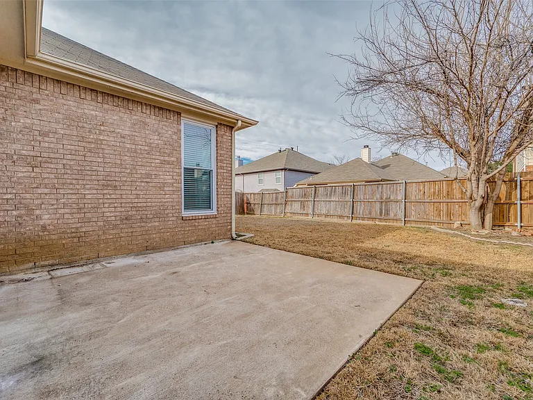 Spacious concrete patio with a brick exterior, framed by a wooden privacy fence and a mature tree