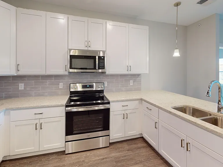 The Dogwood floor plan features a large kitchen featuring quartz countertops, a double sink, stainless steel appliances, and a breakfast bar with pendant lights. The Dogwood floor plan features a large kitchen featuring quartz countertops, a double sink, 