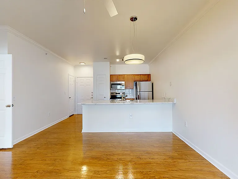 Apartment kitchen with stainless steel appliances, dining and living room with wood-style flooring.