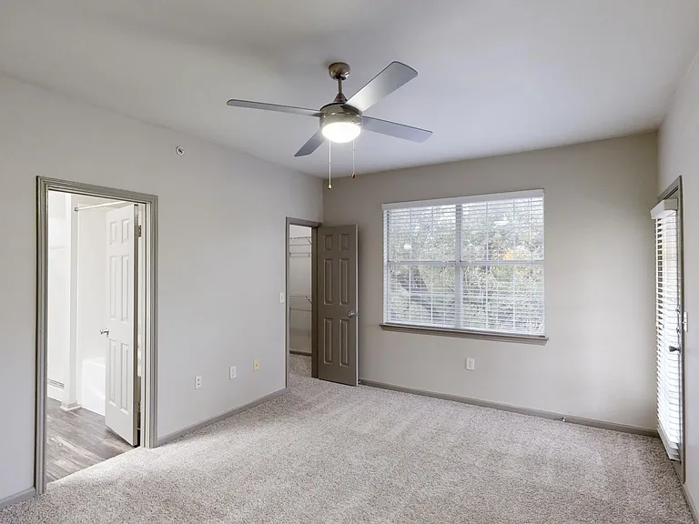 Spacious apartment bedroom with large closet, attached bathroom, and plush carpet flooring.
