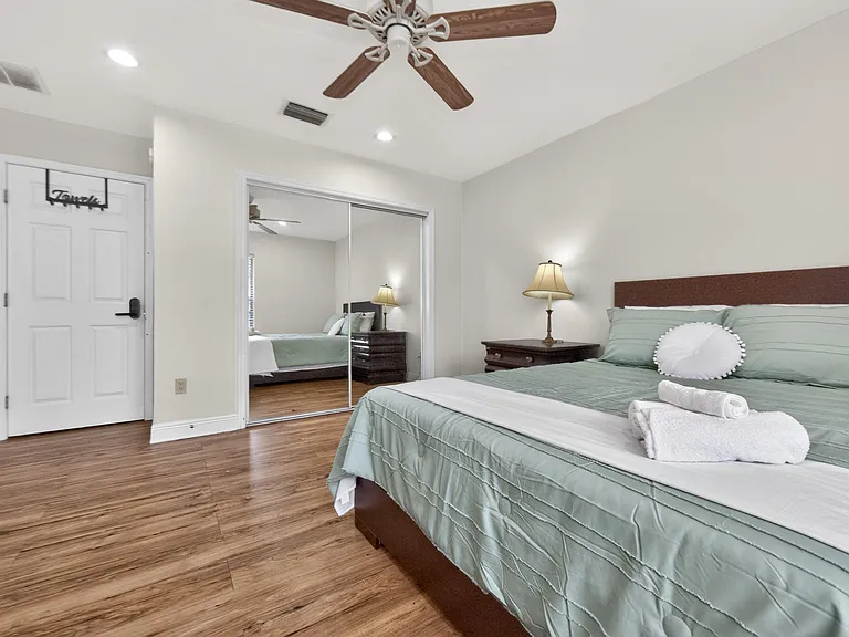 Spacious bedroom with wood-style flooring, ceiling fan, and mirrored sliding closet doors for ample storage.