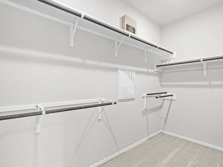 Generously sized primary walk-in closet with multiple hanging rods and shelving on three walls AA?A? ample storage for any wardrobe.\