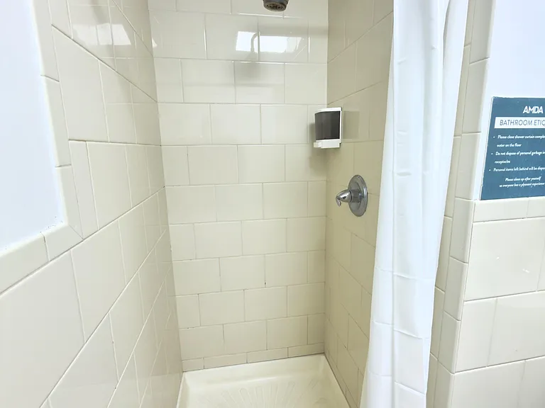 Tile-lined shower stall with a curtain rod and mounted dispenser, offering a simple, easy-to-clean bathing area.