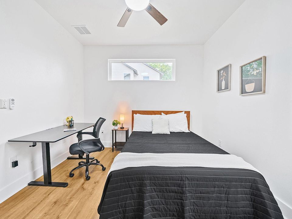 Private bedroom with a full bed, dedicated desk workspace, ceiling fan, and high window for natural light.