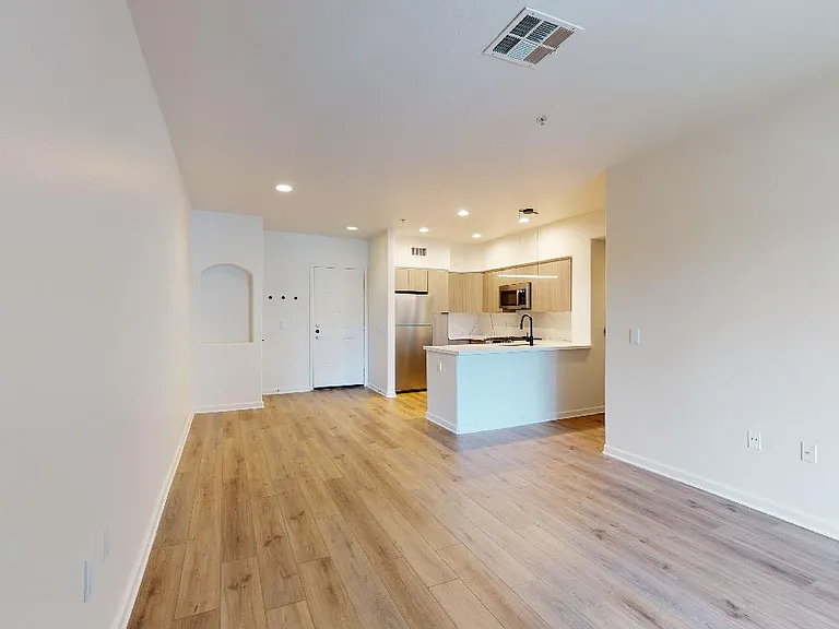 Apartment kitchen with stainless steel appliances, dining and living room with wood-style flooring.