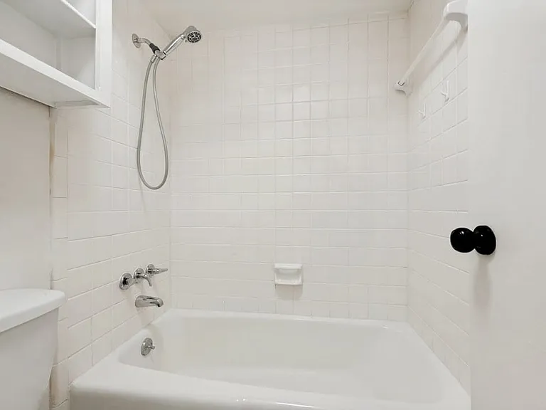 Bathroom featuring a white bathtub, white subway tile surround, chrome fixtures, and an upper storage cabinet