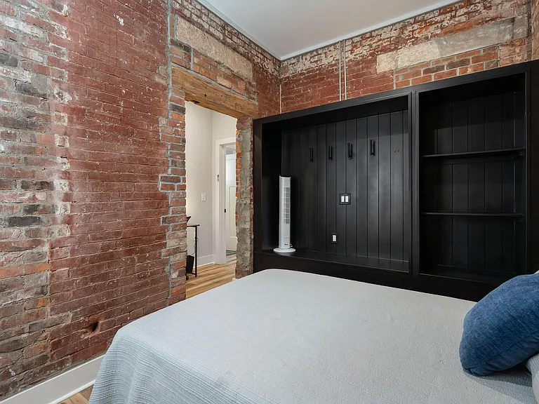 Bedroom featuring exposed brick walls, a built-in storage with shelving, and wood-style flooring.