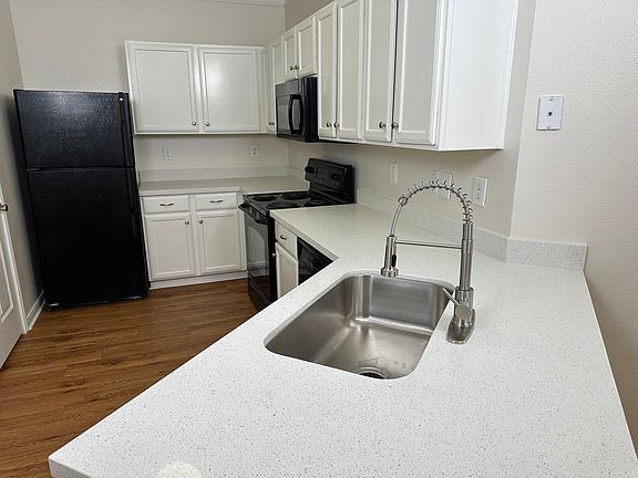 Modern kitchen with quartz countertops, stainless steel sink, and classic white cabinetry, featuring black appliances and elegant wood flooring. Modern kitchen with quartz countertops, stainless steel sink, and classic white cabinetry, featuring black app