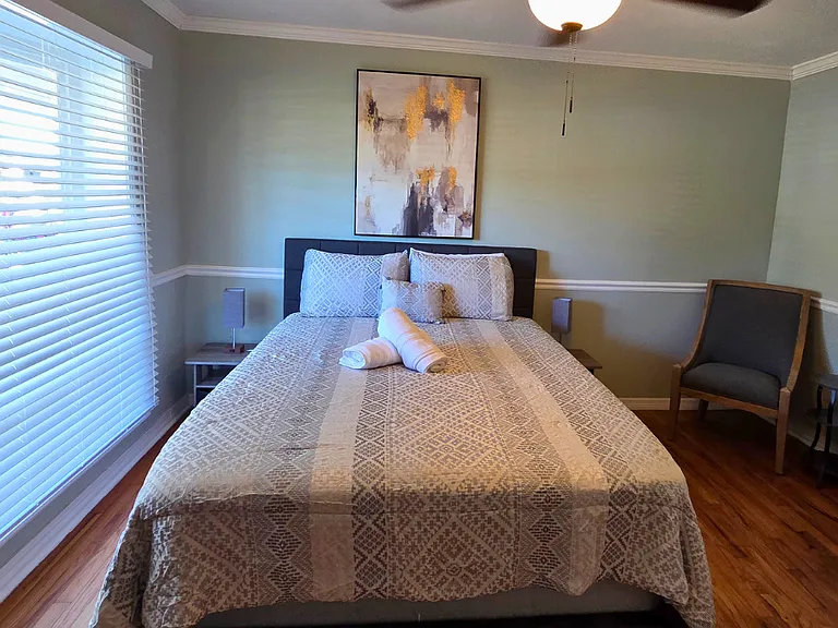 Bright bedroom with large window, beautiful blinds, and wall art.
