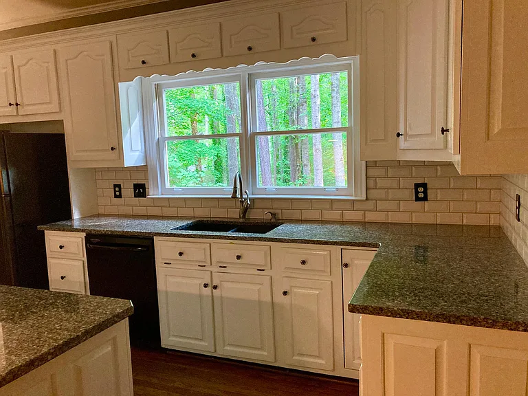 A large white kitchen, granite countertops and a center island offer lots of space. The windows look across a second floor deck and out to a wooded back yard.