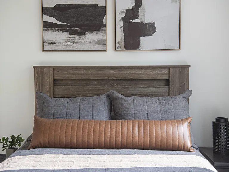 Contemporary bedroom with a stylish wooden headboard, cozy gray and brown pillows, and modern abstract wall art.