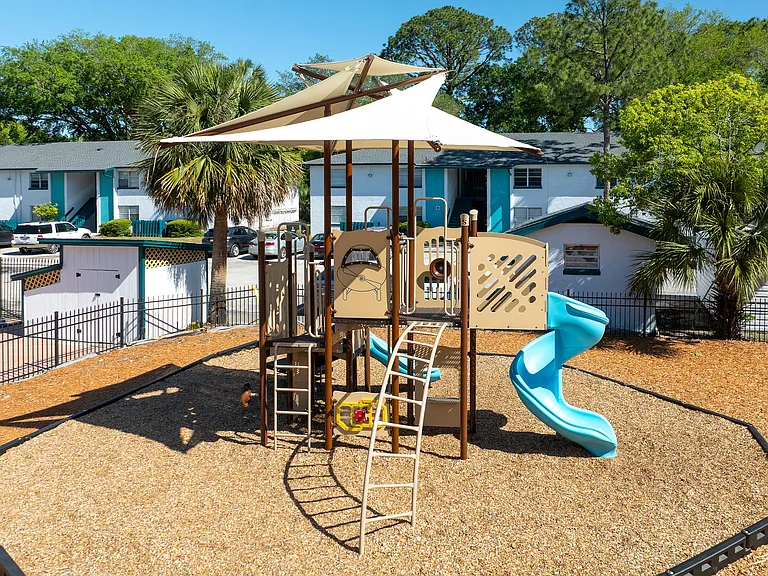 Charming outdoor playground with a modern play structure, vibrant slide, and shade sail, nestled in a lush residential area.