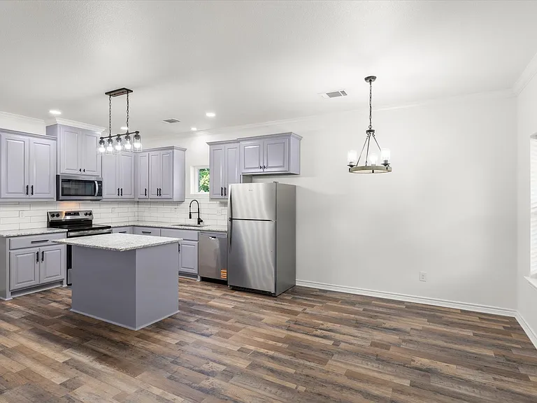 Contemporary kitchen featuring light gray cabinetry, stainless steel appliances, a center island with a stone-finish countertop, and wood-finish flooring