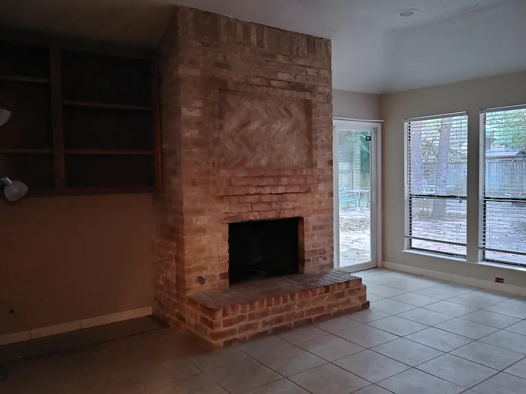 wood burning fireplace in family room overlooking large partially bricked backyard