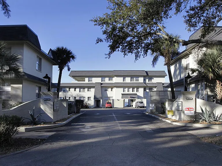 Charming apartment complex featuring elegant architecture and landscaped surroundings, with for rent signs visible at the entrance.