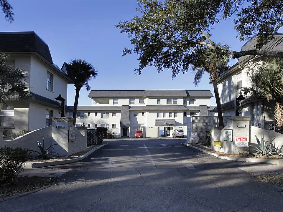 Charming apartment complex featuring elegant architecture and landscaped surroundings, with for rent signs visible at the entrance.