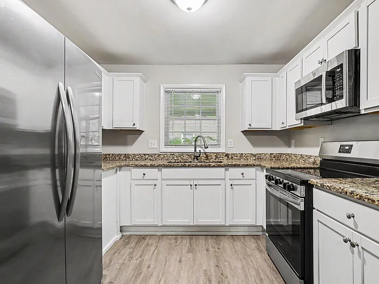 U-shaped kitchen with granite-look counters, ample white cabinetry, and stainless steel appliances plus a window over the sin