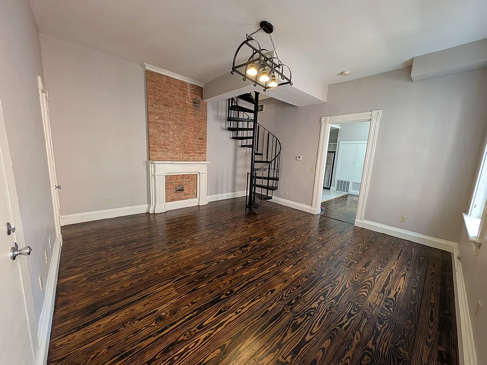 Large living room with exposed brick and hardwood floors. Spiral staircase goes up to the second floor bedrooms.