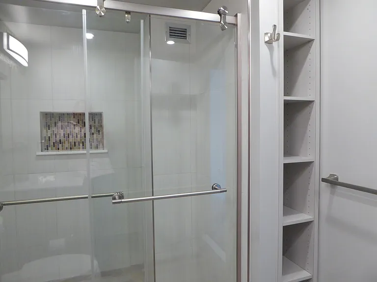The bathroom features a large step-in shower with stylish glass sliding doors, nickel finish accessories, and convenient built-ins.