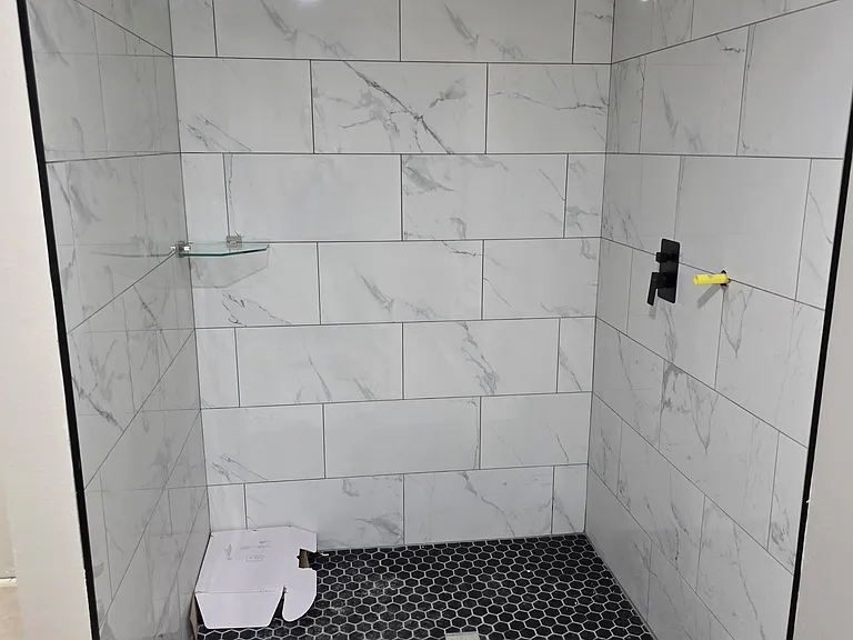 Primary bathroom shower update in progress with marble tile and black fixtures.