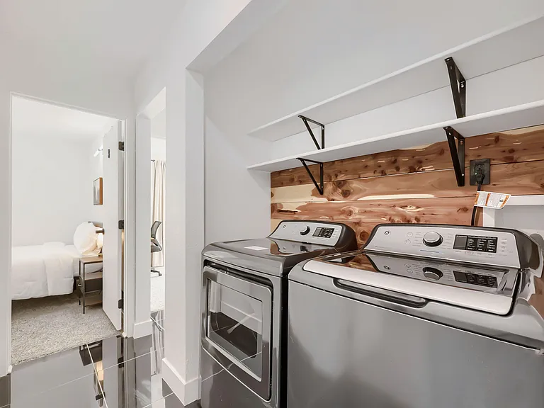 Dedicated laundry nook for Rooms 1-4 with side-by-side washer and dryer plus open shelving for detergents and storage.