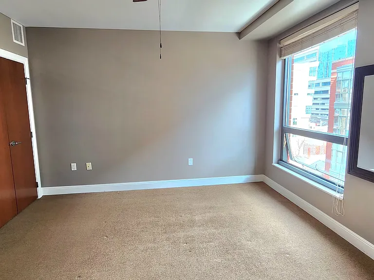 View of the bedroom from the west wall. Windows look onto the neighboring building and the plaza.