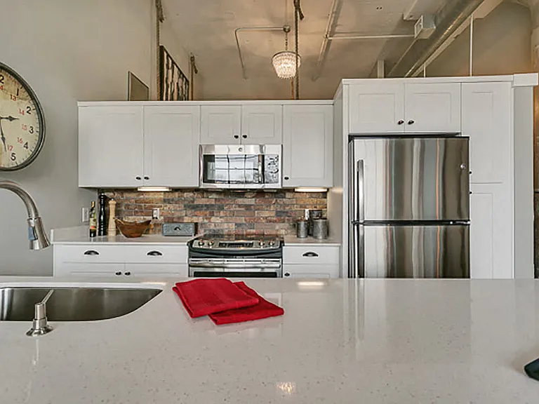 Modern kitchen with white cabinets and brick style backsplash, with white quartz countertop