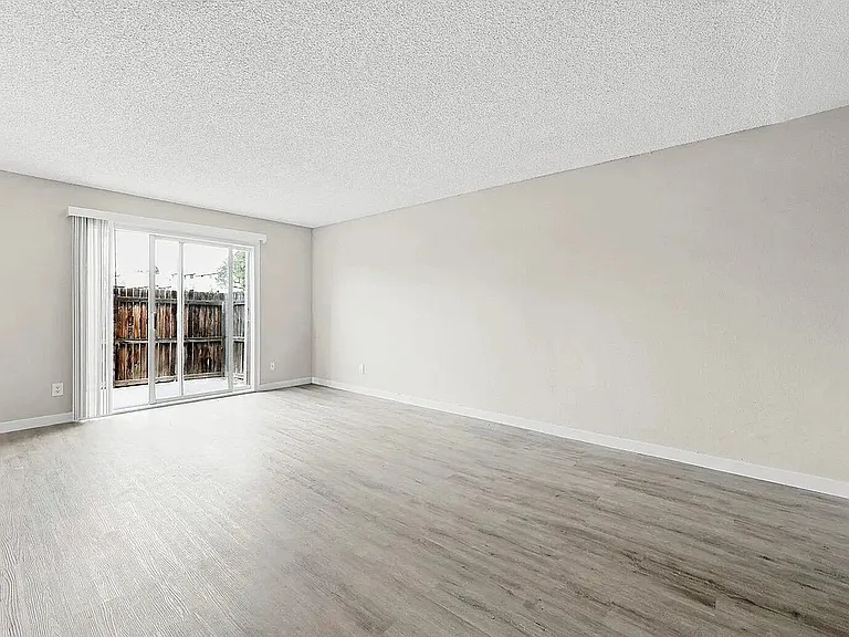 Bright, spacious living area with elegant hardwood floors and large sliding glass doors leading to a private patio.