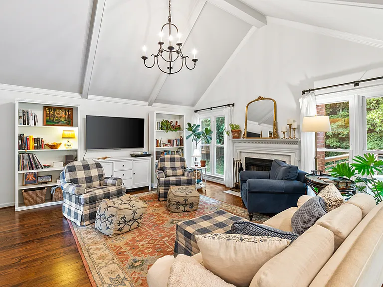 Spacious and bright living room with vaulted, beamed ceilings, a Smart TV, a fireplace, and windows looking out to the wooded backyard.
