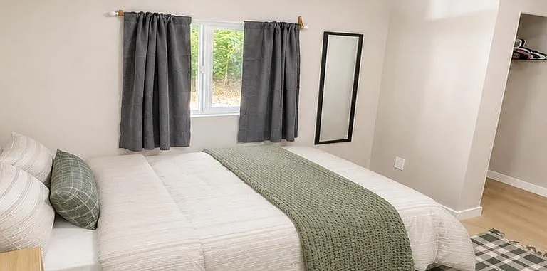 Spacious bedroom featuring a full-size bed, window with curtains, and convenient open closet nook for easy storage.