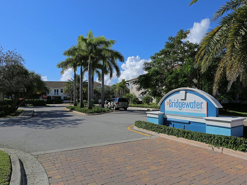 Inviting entrance to Bridgewater at Lake Osborne with palm trees and a sunny, welcoming atmosphere.