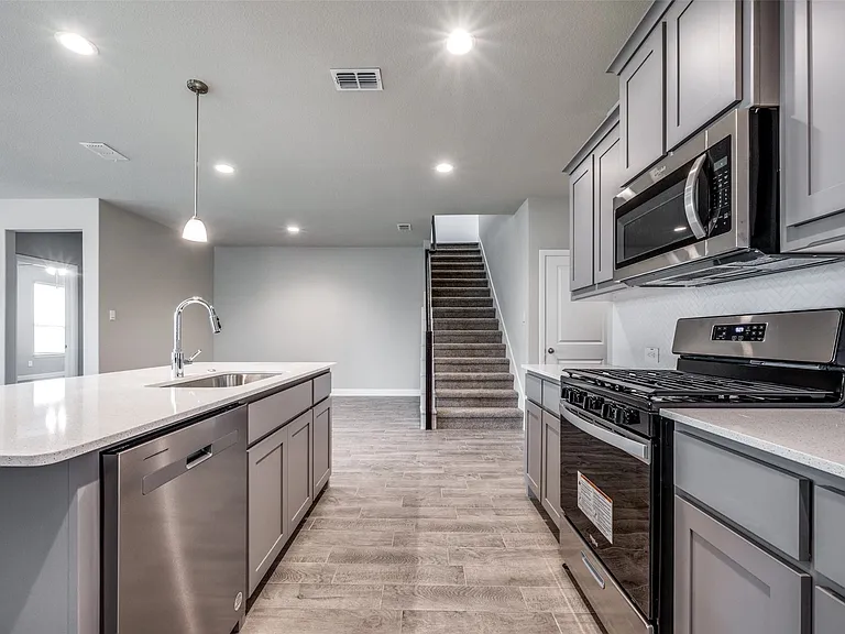 Kitchen with light hardwood / wood-style floors, hanging light fixtures, stainless steel appliances, an island with sink, and sink
