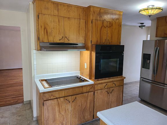 Kitchen with cook top, hood fan/light, wall oven, custom cabinets, refrigerator, tile floor